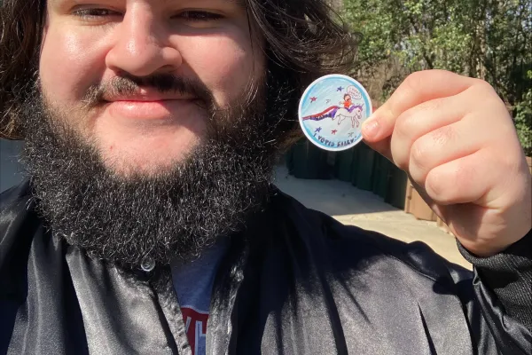 photo of smiling bearded person holding an early voting sticker 