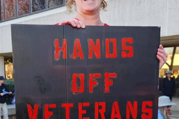 photo of libby manly holding a protest sign that reads "hands off veterans"